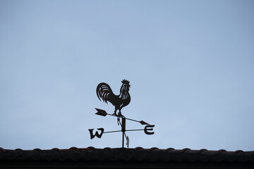 The old wind vane with a rooster symbol icon on the roof, traditional technology equipment for forecast and measuring windy weather in the air, vintage decoration, aiming wind direction instrument. - obrazy, fototapety, plakaty