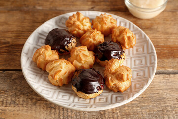 Plate with delicious eclairs on wooden background, closeup