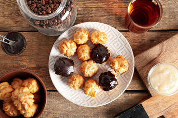 Plate with delicious eclairs on wooden background