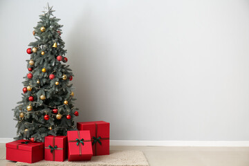 Christmas tree with gifts near light wall