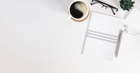 Flat lay notebook, eyeglasses, potted plant and cup of coffee on white table. Top view with copy space.