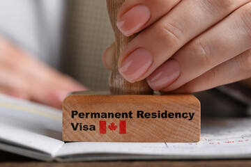 Woman stamping document at wooden table, closeup. Permanent residency visa in Canada