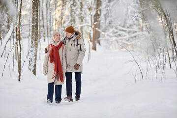 Full length portrait of happy senior couple enjoying walk in winter forest and looking at each other, copy space - Powered by Adobe