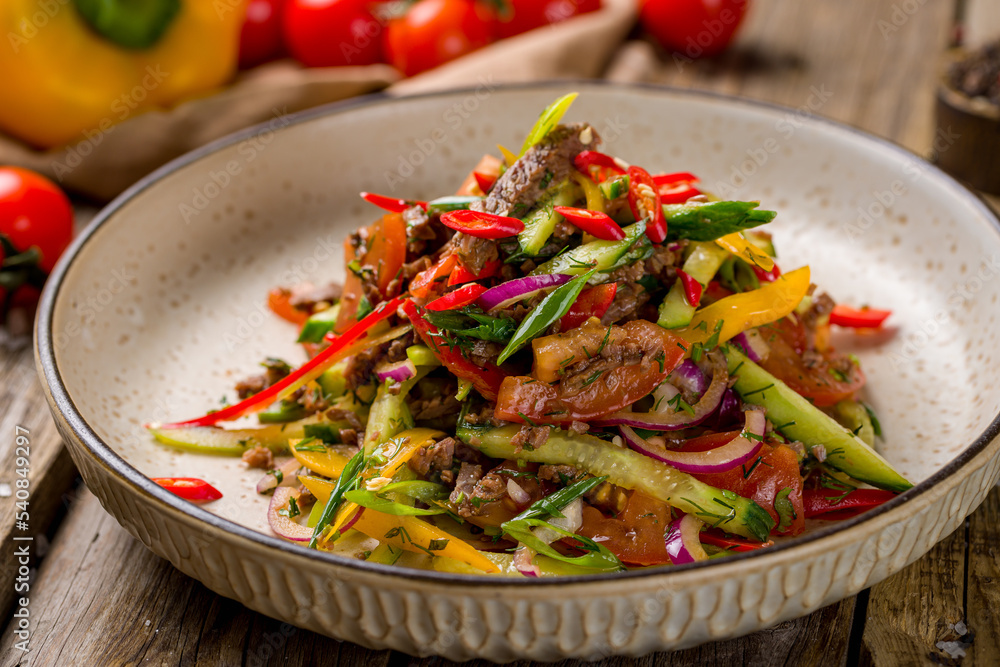 Poster asian salad with beef, vegetables and spicy pepper on blue uzbek plate macro close up on old wooden table