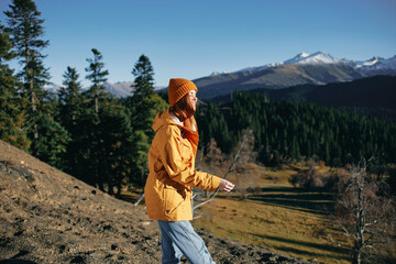 Naklejka premium Woman full back hiker running on the mountain looking at nature happiness overlooking snowy mountains and trees in yellow raincoat travel and hiking in the mountains at sunset freedom