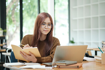 Woman learning online using laptop and writing notes.