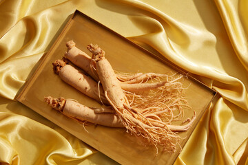 Golden silk background with fresh ginseng in a gold tray.