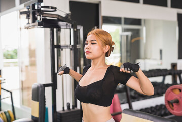 Fototapeta na wymiar A slim and sexy asian woman in a black crop top does dynamic chest stretch before a workout session at the gym.
