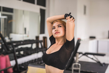 A slim and sexy asian woman in a black crop top does overhead tricep stretches before a workout session at the gym.