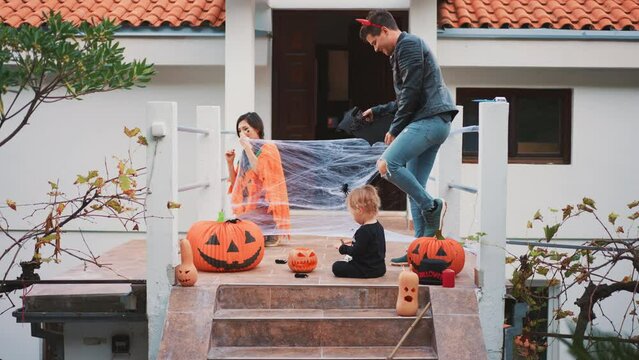 Happy multiethnic family - mother, father and little son celebrate Halloween at home at background of decorated with pumpkin lanern house. People decorating a house. Traditional fall atmosphere