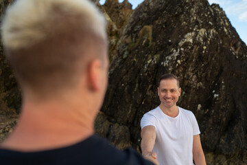 gay couple arm outstretched looking at each other with smile and rocks in background