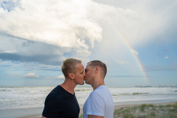 gay couple kissing with rainbow at beach medium shot