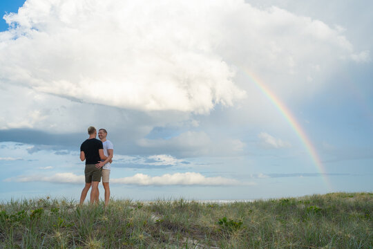 gay couple hugging with rainbow at beach