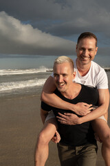 Fototapeta na wymiar Gay couple piggy backing on beach smiling close up