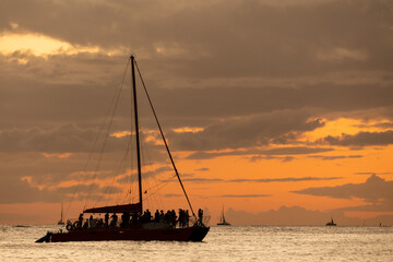 Incredible sunset on Waikiki Beach with sail boat silhouette. Sunset sailing in Hawaii.  