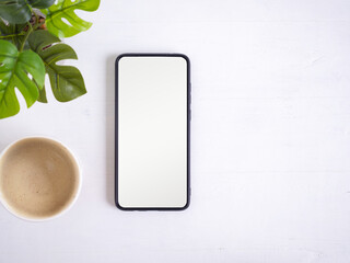 Top view, Smartphone with blank screen and hot coffee cup, plant on white wooden. Flat lay, space for your text..