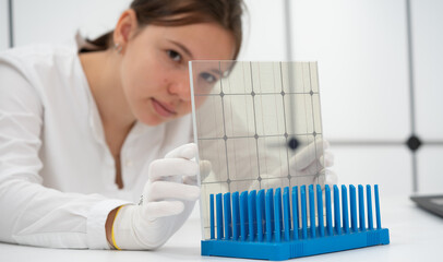 young woman controls the quality of transparent solar panels in a renewable energy laboratory - obrazy, fototapety, plakaty