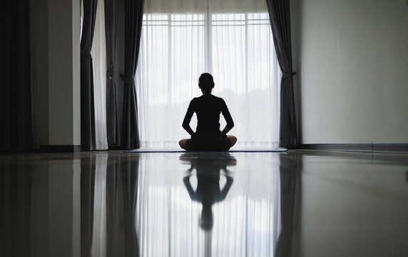 Silhouette Of Young Woman Meditating At Home. Men Practicing Yoga Indoors. Relaxation, Body Care, Meditation, Balance, Fitness,  Workout, Recreation Concept,  Pray.