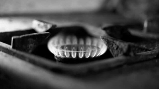 Unstable combustion of gas in the burner of an old gas stove in a deplorable state. A black and white video of a burning natural blue fuel in a rural slum. Low quality of life, poverty and heating