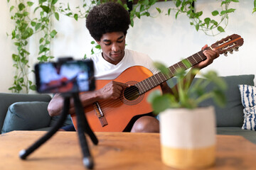 African American guitar teacher filming himself with mobile phone pointing at strings showing...