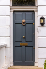 Subdued blue front door, exterior walls are white stone with a light fixture, door knocker and mail slot. England