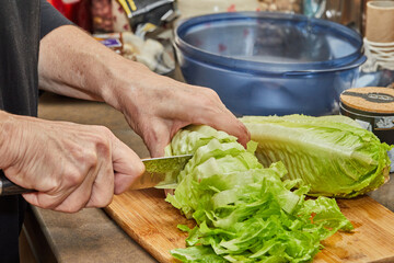 Chef cuts lettuce on wooden board in the home kitchen