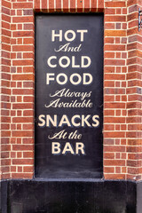 Sign saying hot and cold food, snack at the bar. Letterpress typography, black paint and brick wall. 