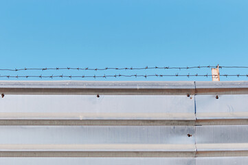 Barbed wire on a metal fence against a blue cloudless sky. Copy space