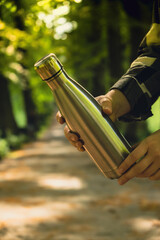 Close-up of Unrecognizable female hand holding Water bottle. Reusable steel thermo water bottle in...