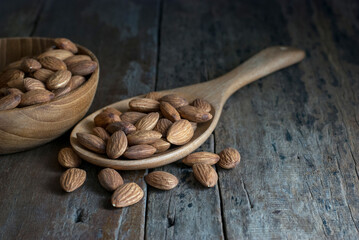 On a rustic hardwood floor, almonds in a wooden ladle and a wooden bowl.