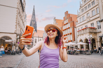 Happy tourist girl taking selfie photo while visiting Prinzipalmarkt street and admiring old town architecture buildings in Munster, Germany