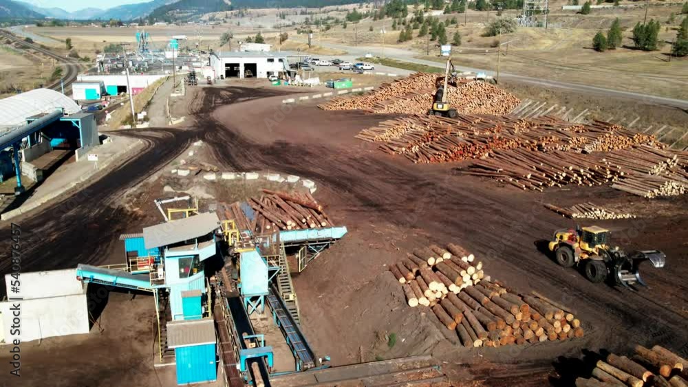 Poster dolly forward zoom drone shot of heavy equipment log loader moving in frame with view of sawmill pro