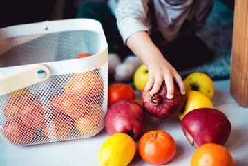 Toddler playing with fruit indoor on the floor, picking, sorting and putting into basket.