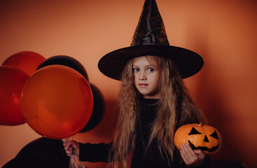 Excited cute little witch girl in a hat with a pumpkin and orange and black balls. child in a...