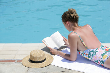 Portrait of beautiful young woman enyojing hot day reading a book next to the swimingpool. Relaxing summer vacation concept. - Powered by Adobe