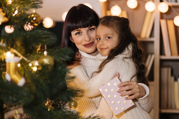 Excited preschool girl, child celebrate New Year at home with loving young mother. Happy mom hugging small daughter with Christmas and congratulate her with gift. Celebration concept.