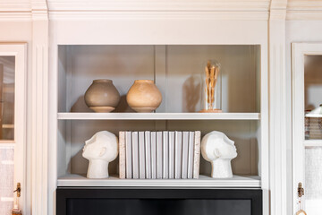 Head shaped bookends with books and clay pot on a shelf indoors. Interior design.