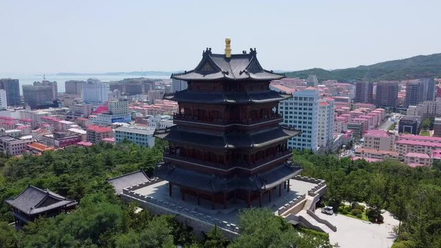 Aerial cinematic complete orbit of the Huancui lou pagoda with blue sky and breathtaking background in Weihai city, China.