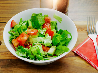 Light meal with freshly cut salad and tomato and cream on a wooden table fork and knife on a red serviette.