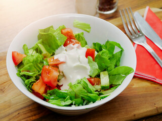 Light meal with freshly cut salad and tomato and cream on a wooden table fork and knife on a red serviette.