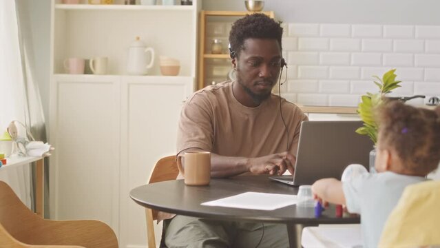 African American father with cute toddler girl working on laptop from home trying to concentrate on work