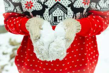 Woman in Christmas sweater and mittens holds snow outdoor