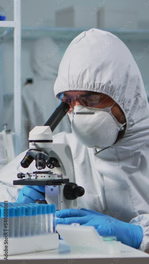 Aufkleber vertical video: close up of scientist looking through a microscope wearing ppe suit in equipped lab.