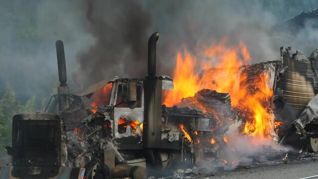 An 18 wheeler semi tractor truck burns uncontrollably on a forested highway