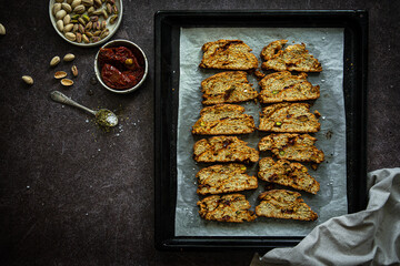 Homemade savory biscotti with dried tomatoes, pistachios, parmesan and aromatic herbs on baking tray.
