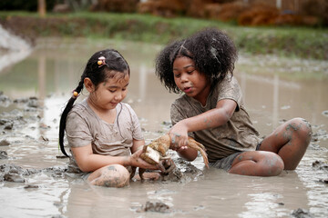 Two happy children child girl catching big frog in the large wet mud puddle on summer day.