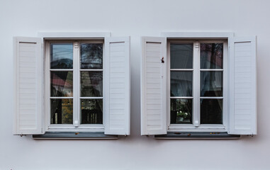 2 okna z białymi framugami na białej ścianie. 