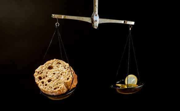 A balance scale with piece of bread on one pan and Euro coins on the other pan. Lever scale with bread and coins on dark background. - Powered by Adobe