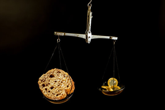A balance scale with piece of bread on one pan and Euro coins on the other pan. Lever scale with bread and coins on dark background.