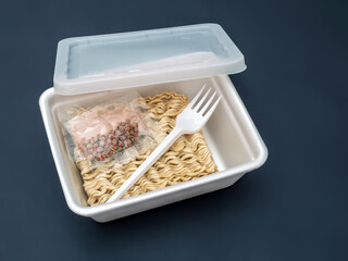 Dried block of instant noodle with seasoning sachets and plastic fork  in a polystyrol lunch box...